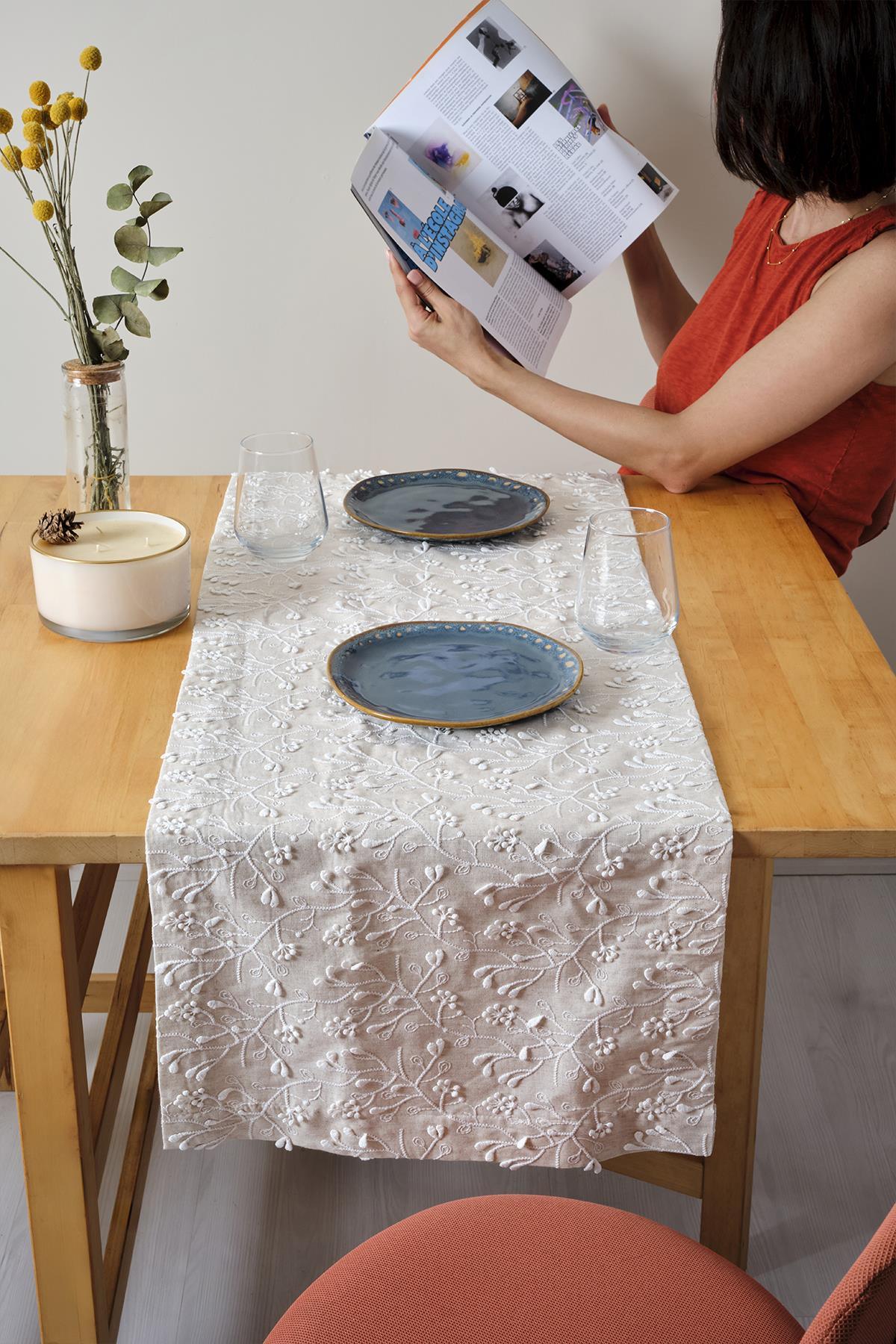 Chemin de table en dentelle crème sur une table en bois, deux assiettes bleues et une décoration de table élégante