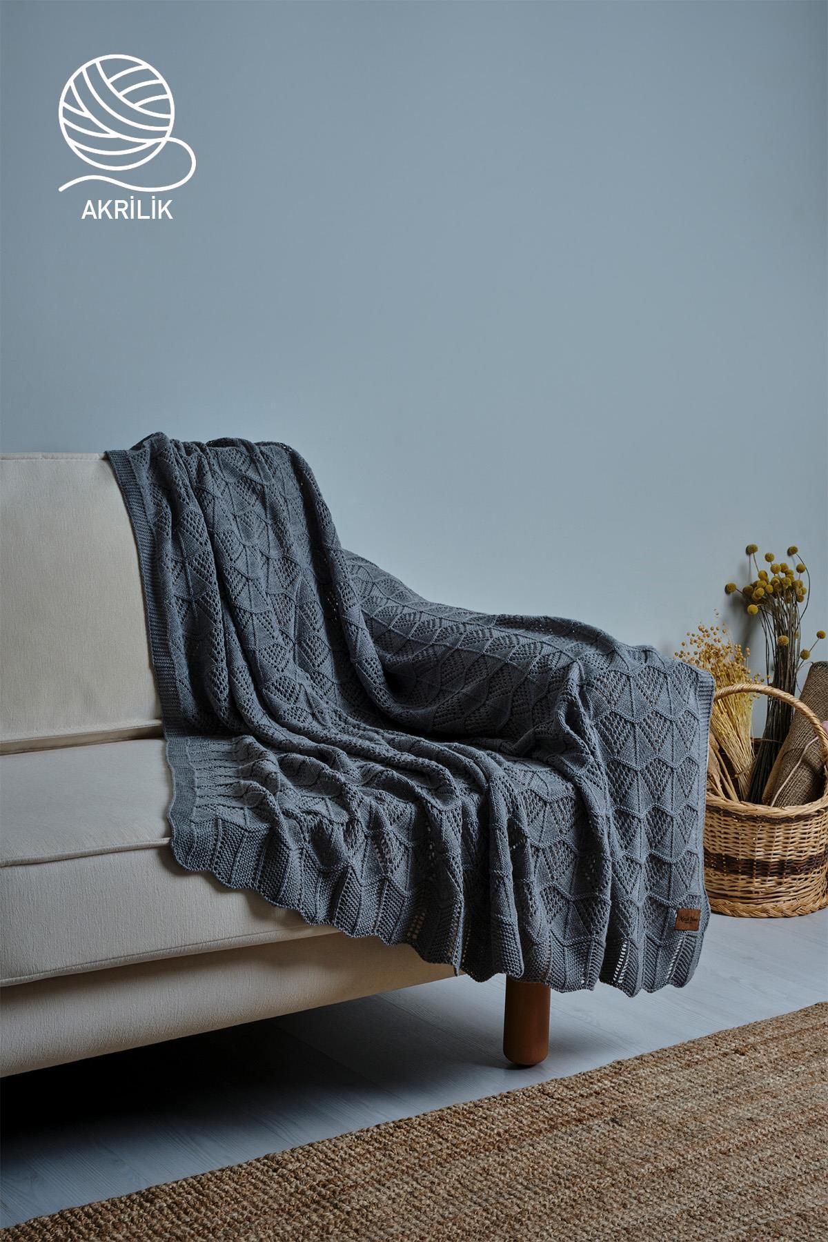 Couverture TV en tricot épais gris acrylique, posée sur un canapé, dans un décor de salon.