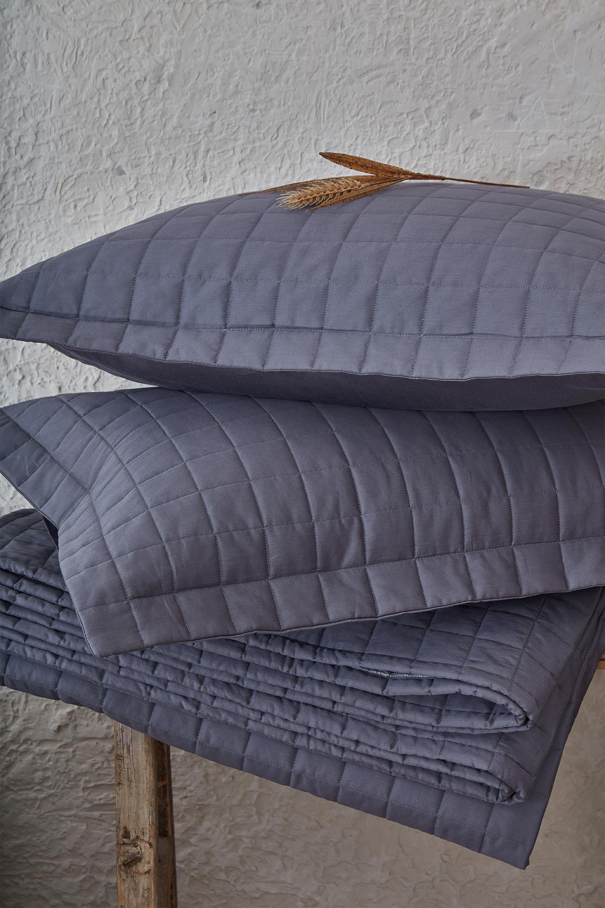 Couvre-lit double gris matelassé avec taies d'oreiller, devant un décor naturel