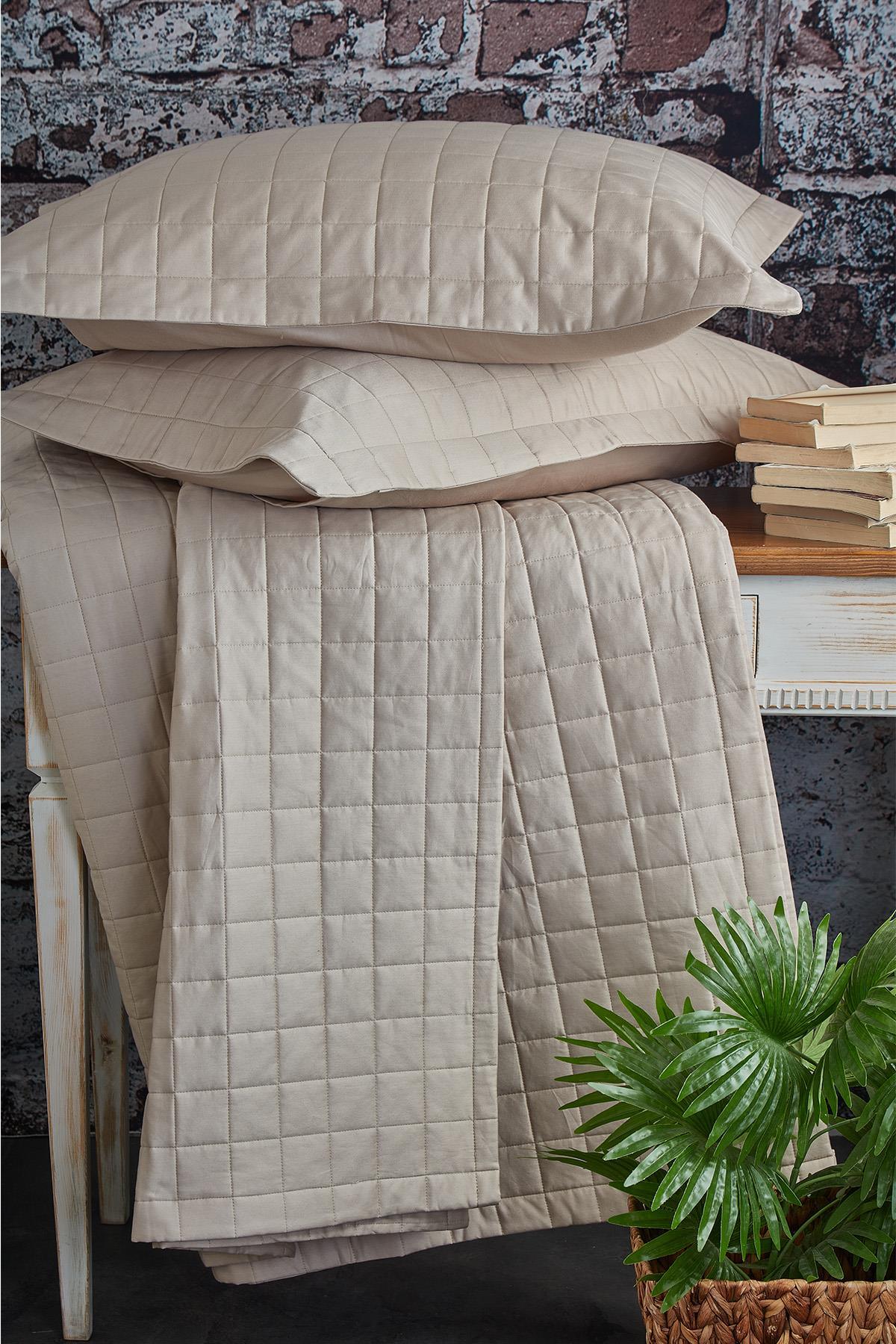 Couvre-lit double matelassé, couleur crème, avec deux oreillers, présenté sur une table