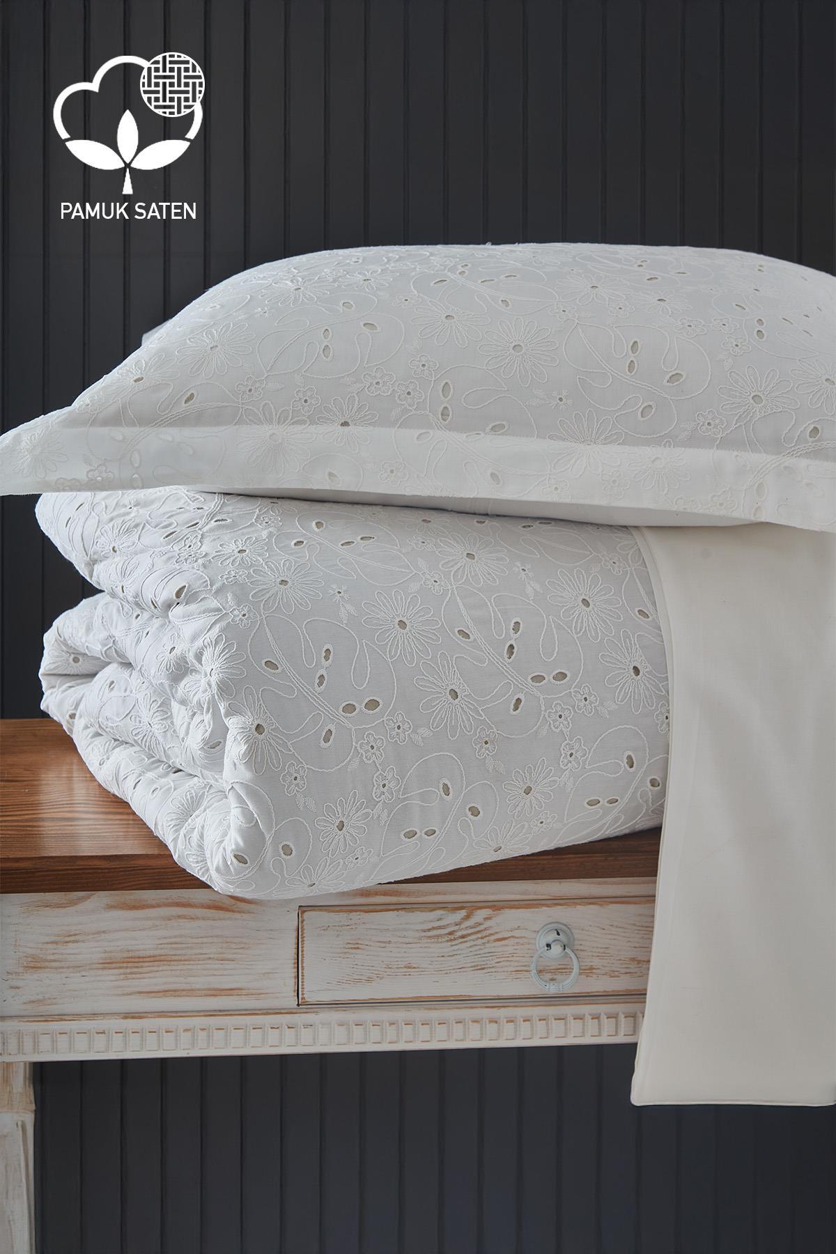 Parure de lit double en satin de coton blanc brodé, pliée sur une table.