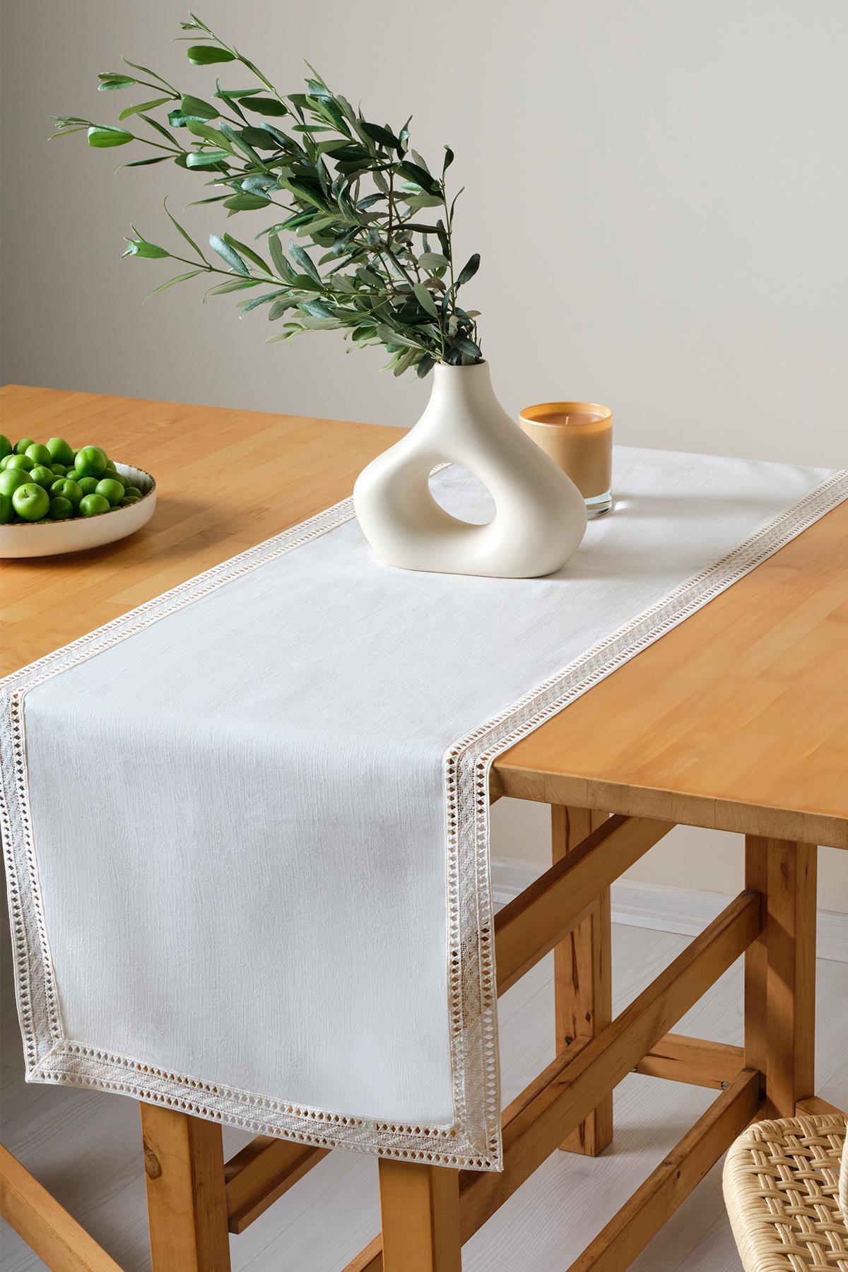 Table en bois décorée d'un chemin de table en dentelle, avec un vase moderne et des prunes vertes dans une assiette