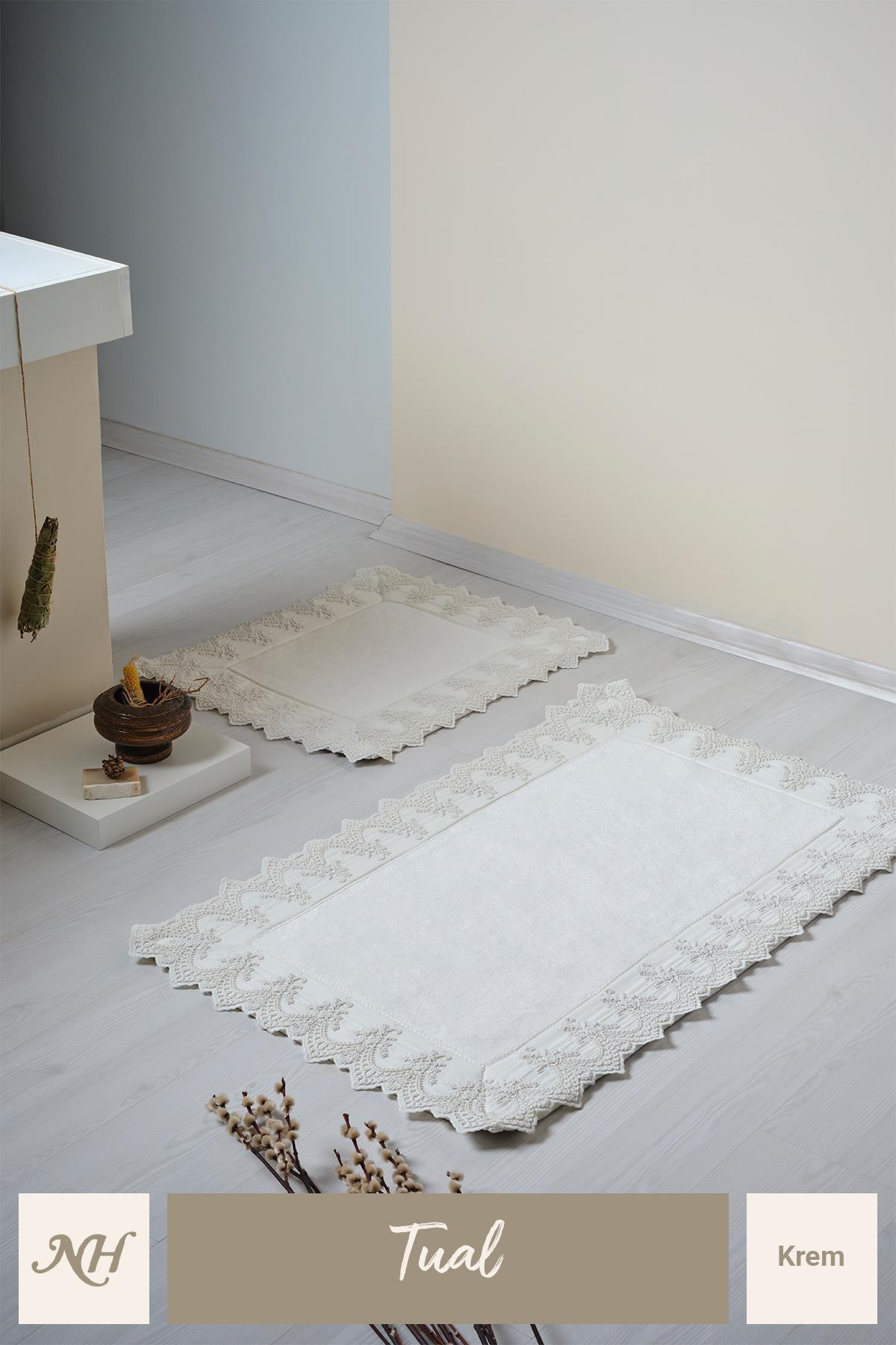Ensemble de deux tapis de bain couleur crème avec broderies en dentelle, sur un sol de salle de bain moderne et élégant