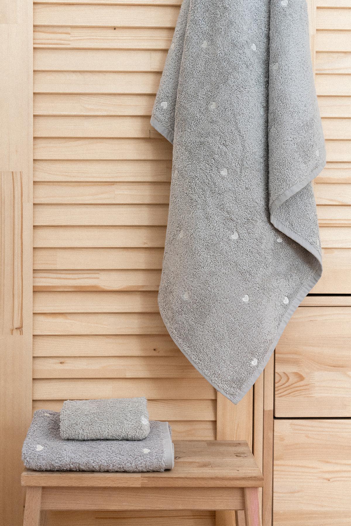 Serviette de bain grise de qualité avec motif cœurs blancs, présentée sur un sol en bois