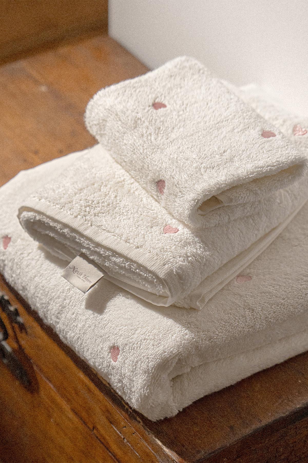 Ensemble de serviettes douces blanches à cœurs roses, pliées sur une surface en bois