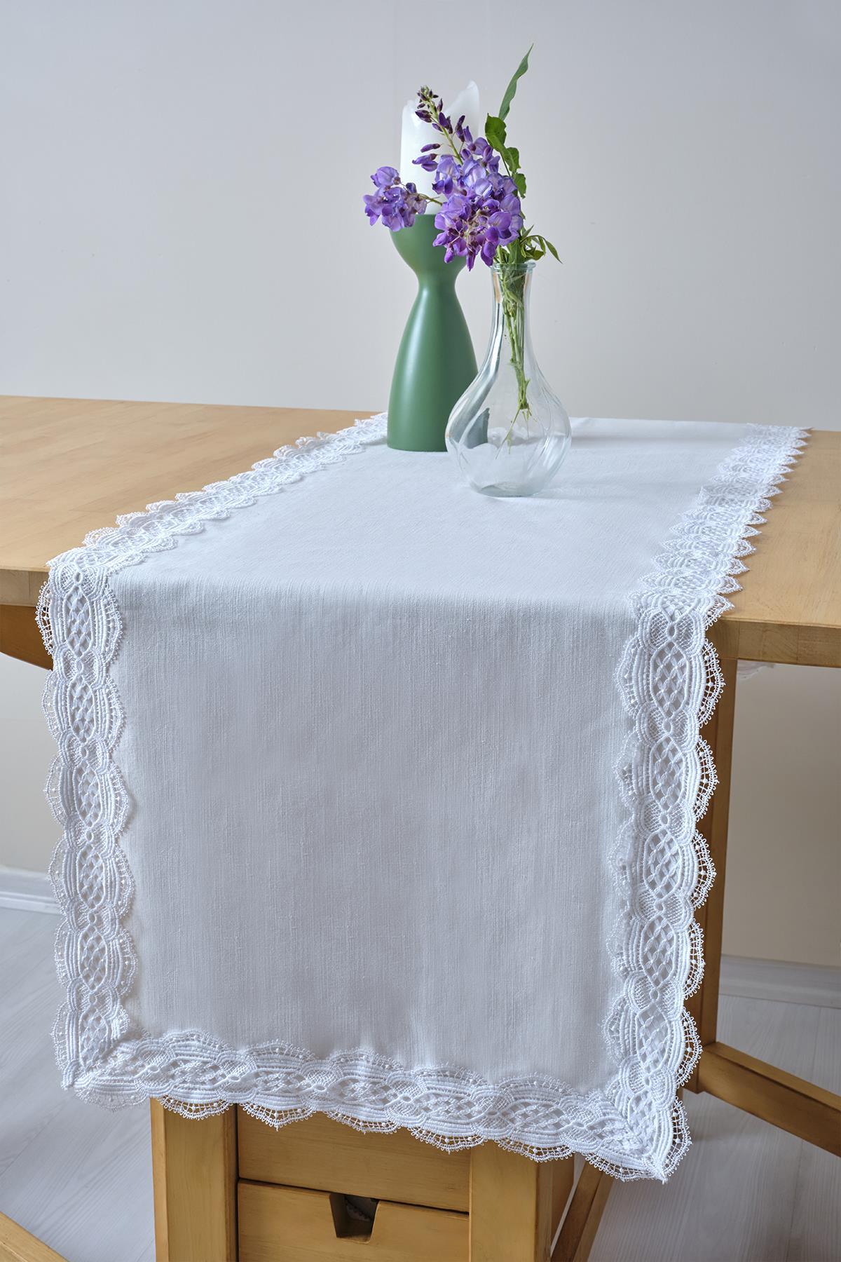 Chemin de table blanc à bordure en dentelle, décoré d'un vase en verre et de fleurs violettes sur une table en bois