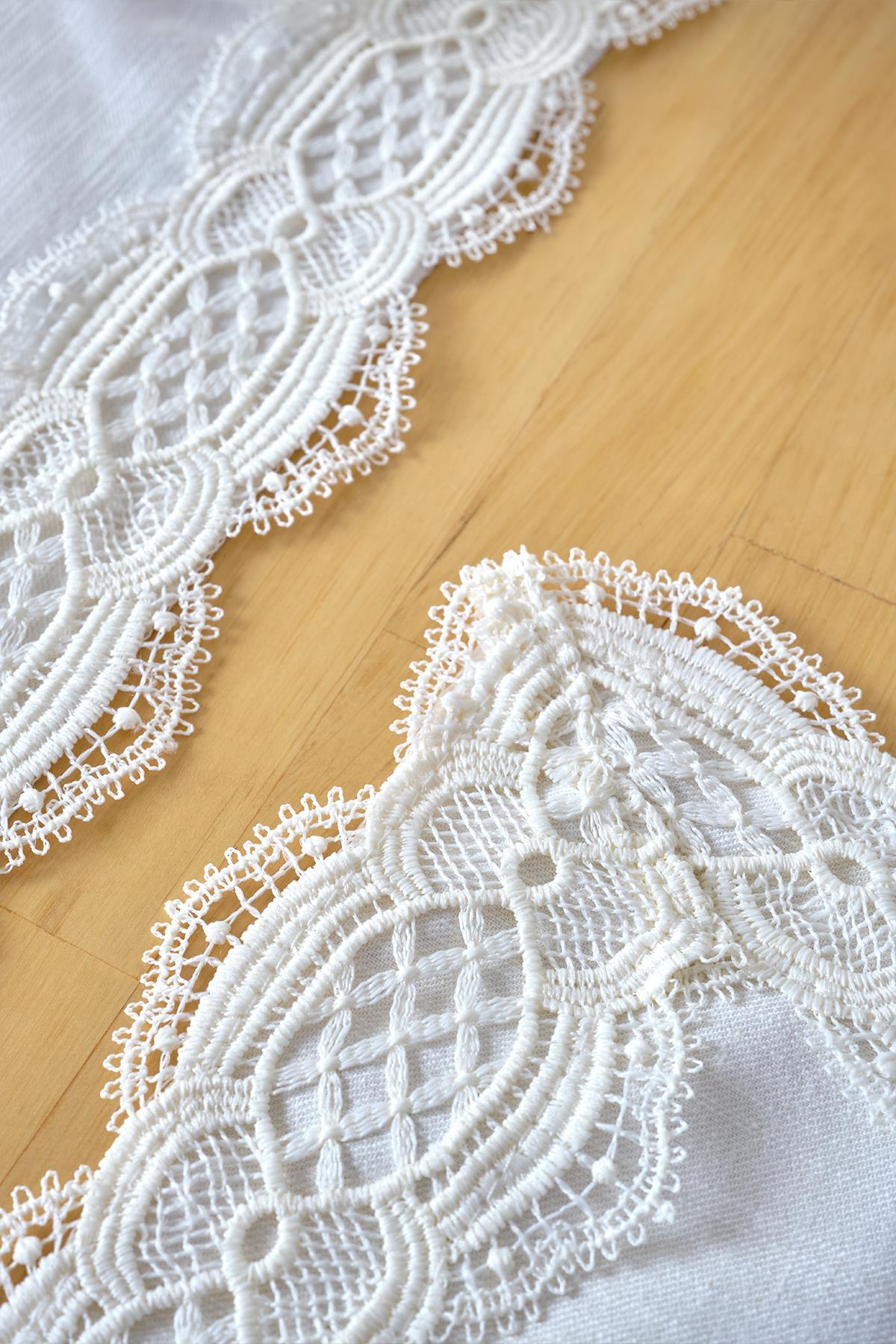 Chemin de table crème avec broderies en dentelle, gros plan détaillé sur un sol en bois