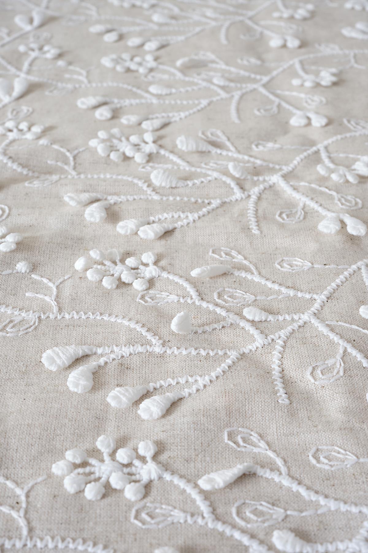 Gros plan sur un tissu brodé à motifs floraux blancs en relief sur fond beige