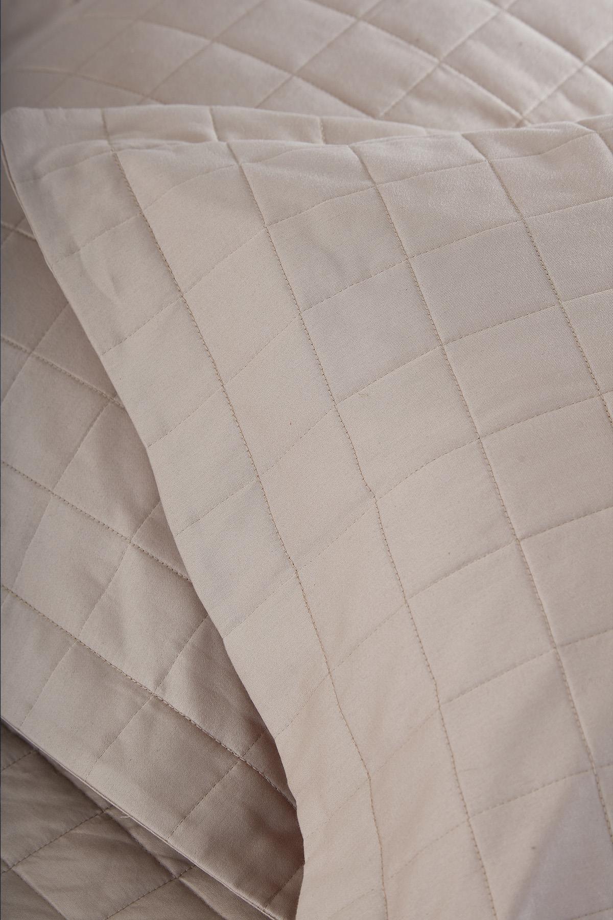 Gros plan sur un couvre-lit double matelassé beige avec taie d'oreiller