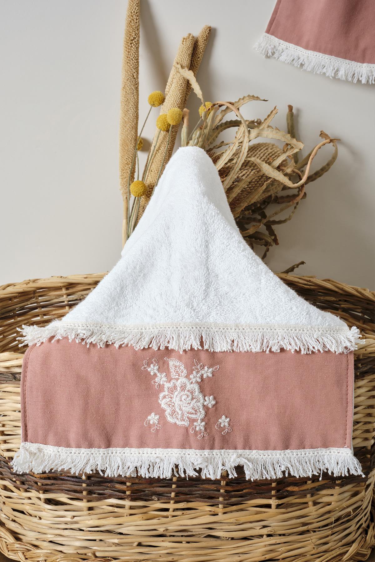 Petite serviette rose en dentelle avec bordure brodée, présentée de manière décorative sur un panier.