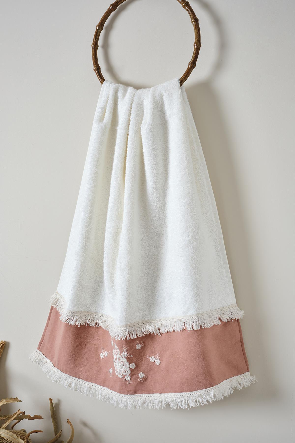 Serviette de bain blanche avec broderies en dentelle rose et pompons, suspendue à un crochet