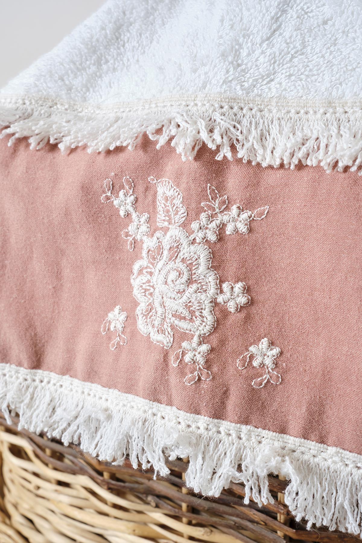Gros plan sur une serviette de bain rose et blanche avec broderies en dentelle et pompons
