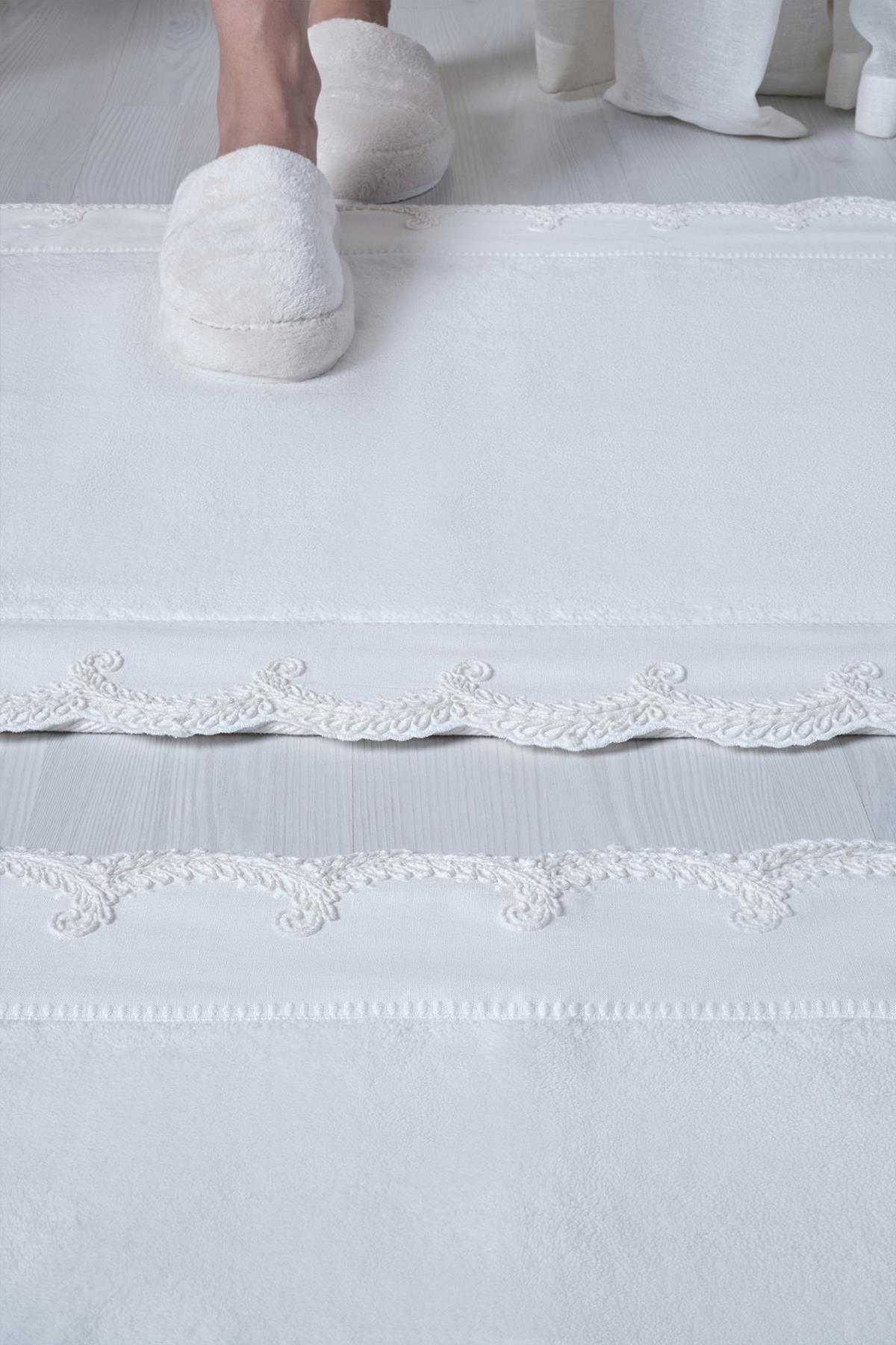 Ensemble de 2 tapis de bain blancs brodés avec détails en dentelle sur le bord, posés sur un sol moderne