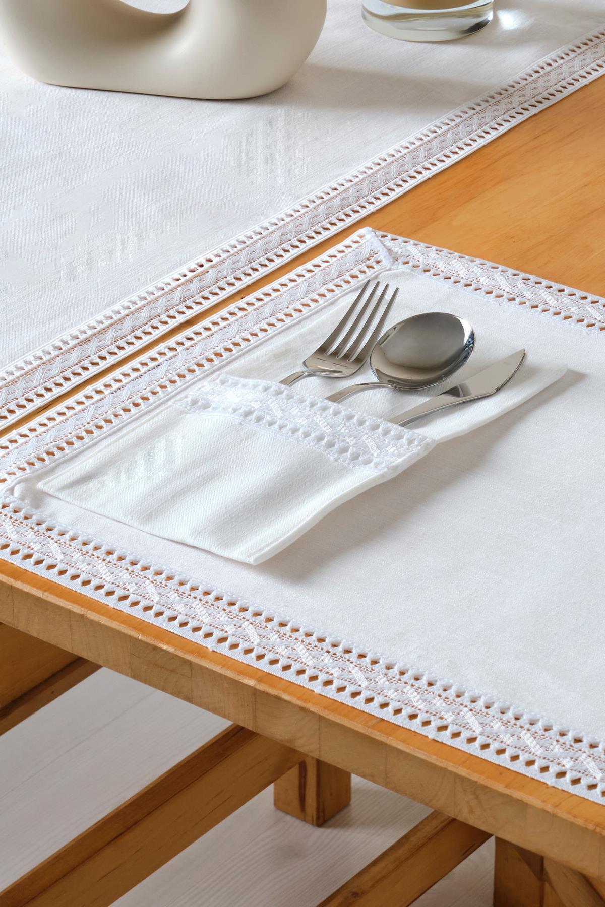 Décoration de table élégante avec une nappe blanche en dentelle et des couverts disposés dans une pochette.